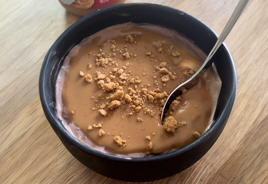 een kom Biscoff overnight oats met een lepel in op een houten achtergrond