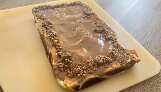 op een plastic plank gepresenteerde Protein biscoff cheesecake op een houten tafel