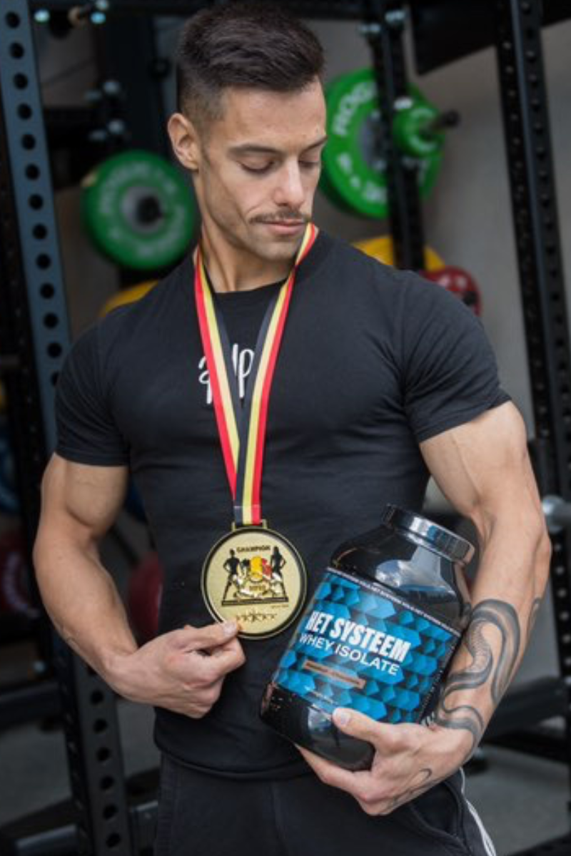 een belgische bodybuilder die als kampioen poseert met een pot whey isolate van het systeem als ambassadeur